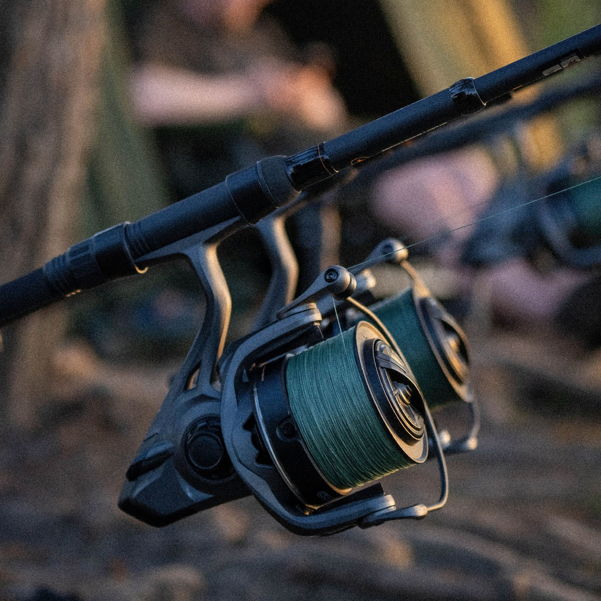 A close-up of a black spinning fishing reel mounted on a fishing rod, with green line spool and a blurred outdoor background.