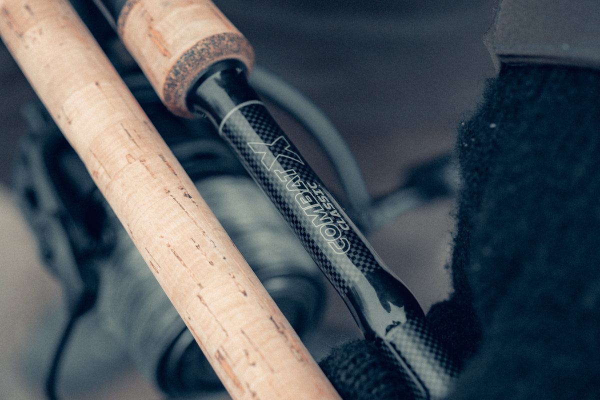 Close-up of a Prologic Combat Classic fishing rod with a black carbon fiber patterned shaft and cork handles, resting on a dark surface.